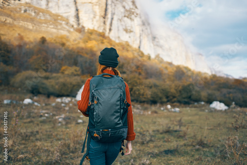 woman in a warm hat with a backpack on her back and in a sweater outdoors in the mountains gesticulate with her hands