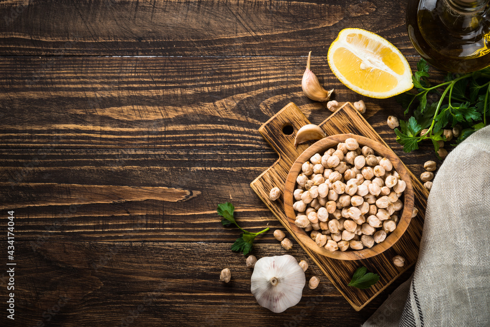 Chickpeas in a bowl with ingredients for cooking hummus at dark wooden table. Top view with copy space. Chickpeas in a bowl with ingredients for cooking hummus at dark wooden table. Top view with copy space.