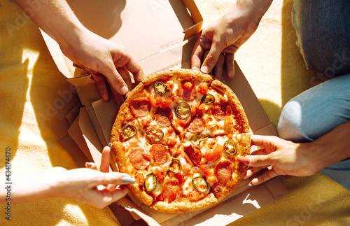 Hands taking slices of pizza close view. Friends eating pizza at the beach. Fast food concept. Beach holiday and summer vacation concept.