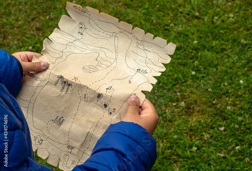 The child's hands hold a pirate map drawn on paper. Play a quest in the fresh air.