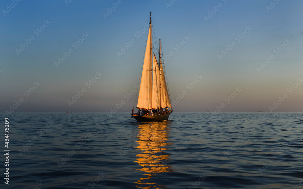 vacationers soaking up the sun on a sailboat  with sails reflecting in the water