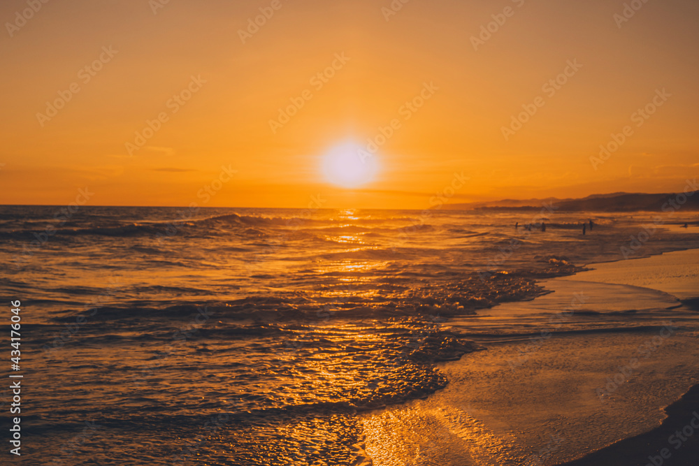 Horizontal photo of a sunset, where you can see the color of the sun reflected in the waves.