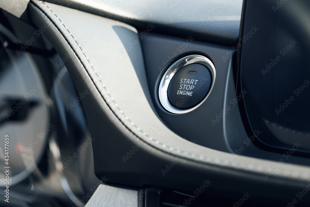 Car Start-Stop Engine Button of a modern car in the interior of the expensive car. Black leather car interior with white stitching. Illuminated dashboard. Luxurious instrument cluster. Close up