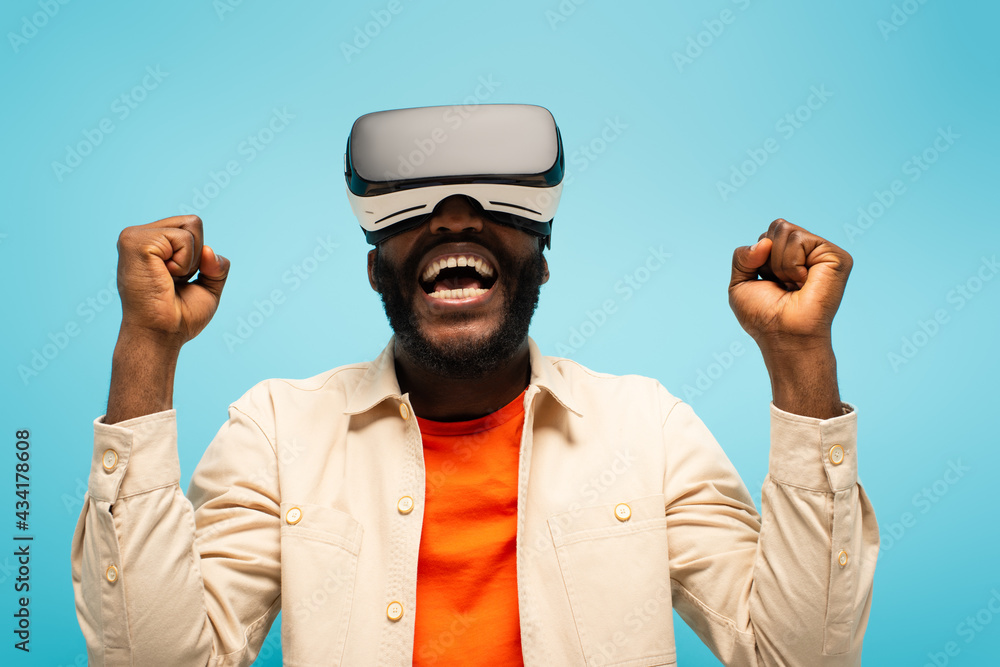Fototapeta premium african american man screaming and showing success gesture while gaming in vr headset isolated on blue