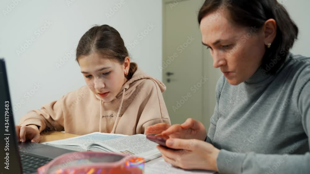 Mother helps cute Caucasian little girl to do homework indoors. A caring tutor gives a private lesson to a schoolgirl. Mom and daughter at the laptop.