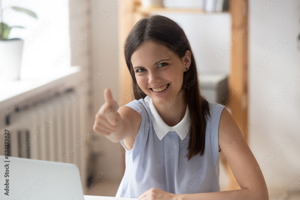 Portrait of happy young Caucasian female employee work on computer in office recommend company employer. Smiling millennial woman show thumb up give recommendation. Employment concept.