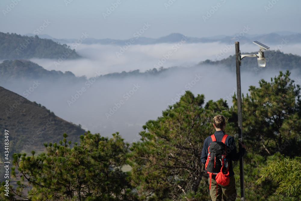 Obraz premium A tourist with a backpack look out over a misty valley landscape