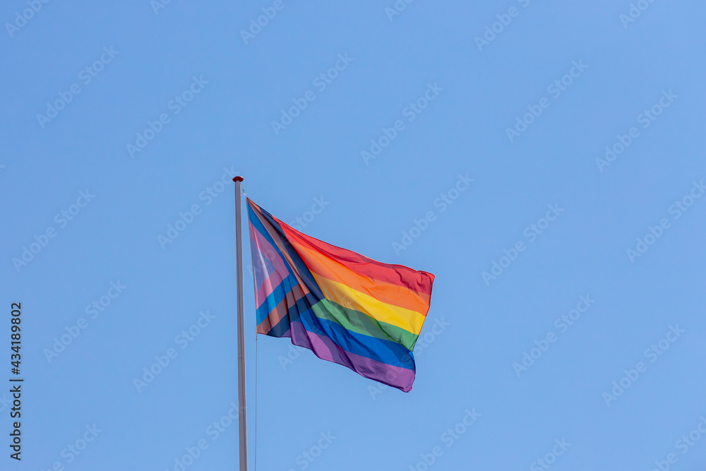 Progress pride flag (new design of rainbow flag) waving in the air with blue sky, Symbol of Gay, Lesbian, Bisexual and Transgender, LGBT community in Holland, Social movements, Amsterdam, Netherlands