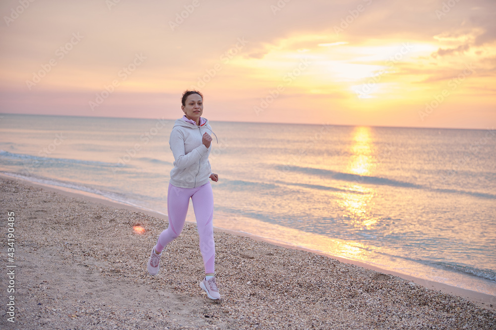 Young athletic woman performing morning jog along the coastline of the sea