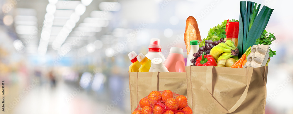Eco friendly reusable shopping bags filled with different goods on a supermarket background