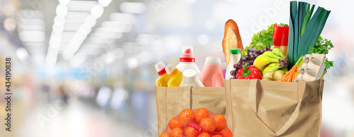 Eco friendly reusable shopping bags filled with different goods on a supermarket background