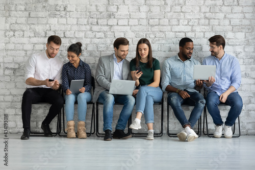 Diverse couples of millennial gadget users sharing content on tablet, smartphone, laptop screens. Group of friends watching and discussing videos together, checking social media news, shopping online