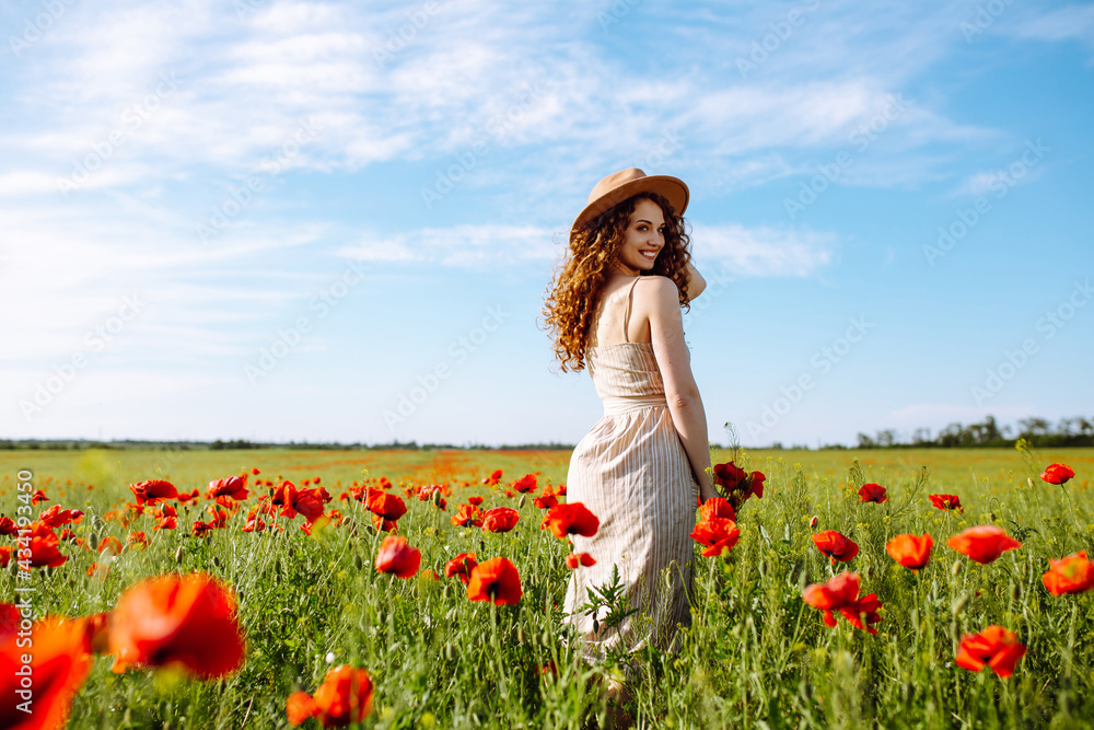Beautiful girl posing in a poppy field. A woman with a hat stands in the middle of flowers. The young girl smiles. Happiness concept. Relaxing on summer poppy flowers meadow. Beautiful girl posing in a poppy field. A woman with a hat stands in the middle of flowers. The young girl smiles. Happiness concept. Relaxing on summer poppy flowers meadow.