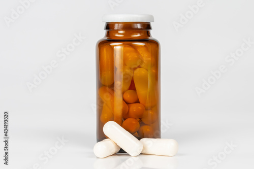 brown glass bottle with white capsules on white background with reflection