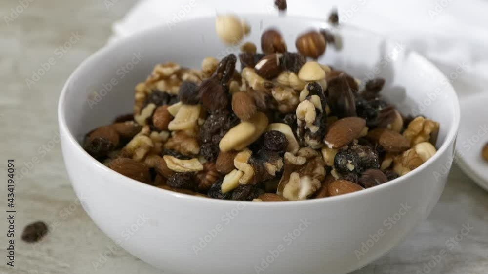 Pouring trail mix with almonds, cashews, pecans and raisins into a white bowl slow motion
Pouring trail mix with almonds, cashews, pecans and raisins into a white bowl slow motion