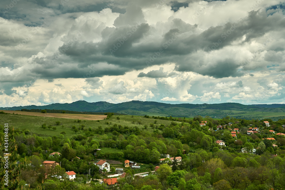 A mountain village in spring, lush green fields and trees, hills and dramatic clouds