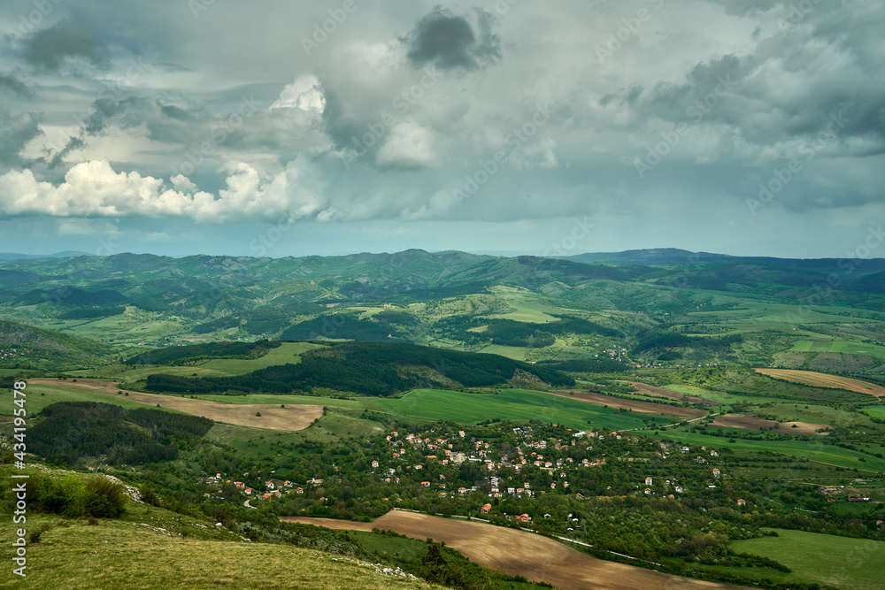 A mountain village in spring, lush green fields and trees, hills and dramatic clouds