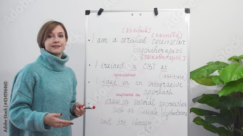 A young English teacher is recording a video lesson in English by taking notes on the chalkboard. Online education and distance learning concept.