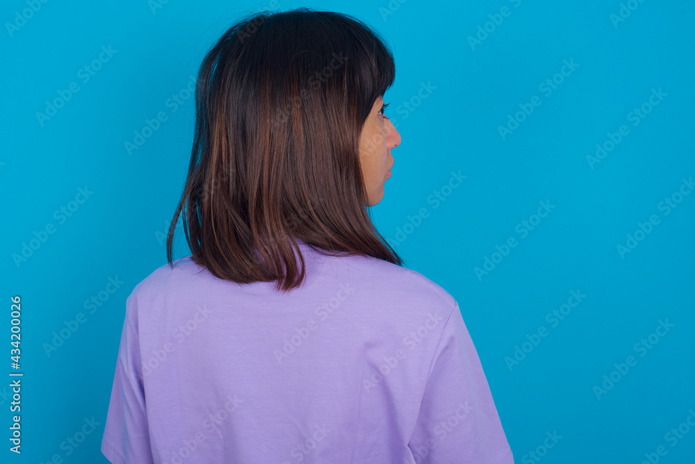 The back side view of a young beautiful asian woman wearing purple t-shirt against blue wall. Studio Shoot. The back side view of a young beautiful asian woman wearing purple t-shirt against blue wall. Studio Shoot.