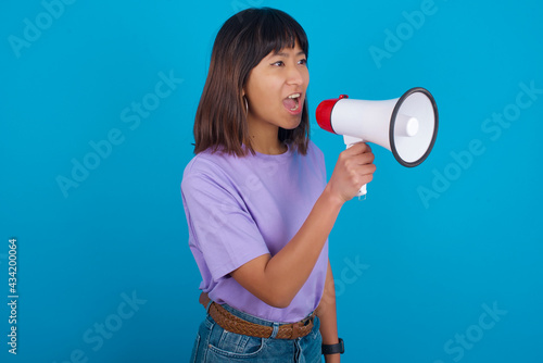 young beautiful asian woman wearing purple t-shirt against blue wall Through Megaphone with Available Copy Space