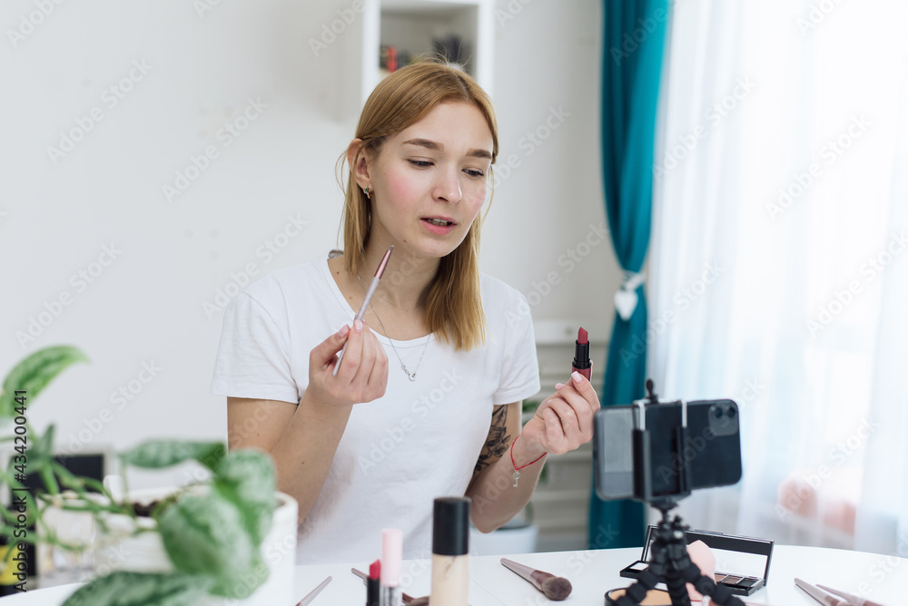 Beauty webinars, makeup classes online. Happy woman vlogger is showing cosmetics products while recording video stream on phone for her internet channel in social media. beauty blog about cosmetics