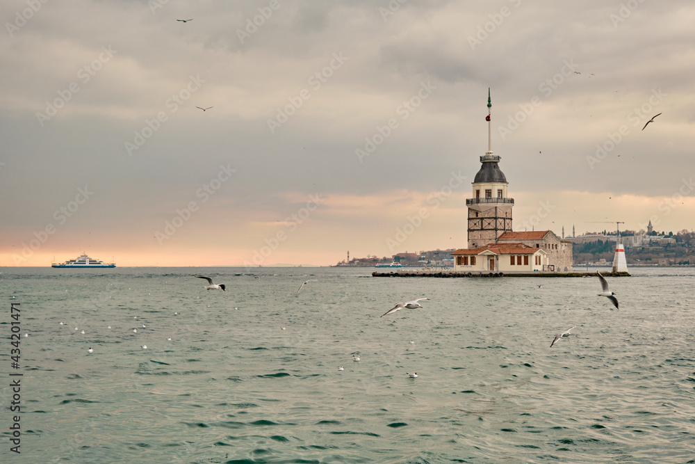 The maiden's tower (kiz kulesi) in istanbul, Turkey during overcast weather with sunshine reflection in bosporus sea.  Groups of seagulls flying on sea. istanbul Turkey 