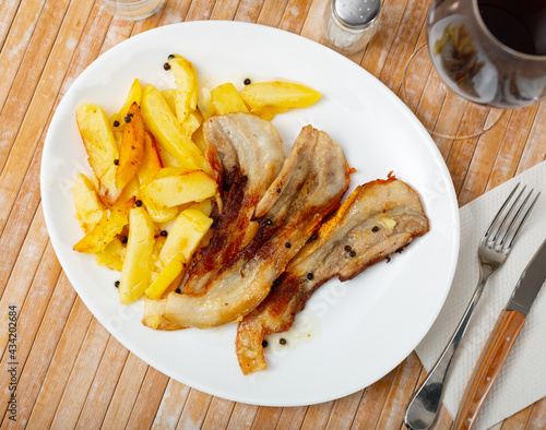 Tasty rustic style dinner with fried potatoes and spicy roasted streaky pork belly strips