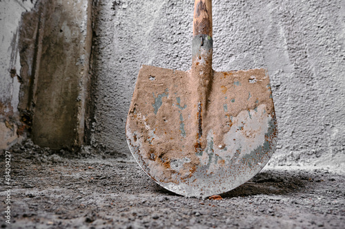 Construction works of plastering. photo taken low angle shovel in front of the recently made plastered wall by concrete. Green colors exist on metal side of shovel.