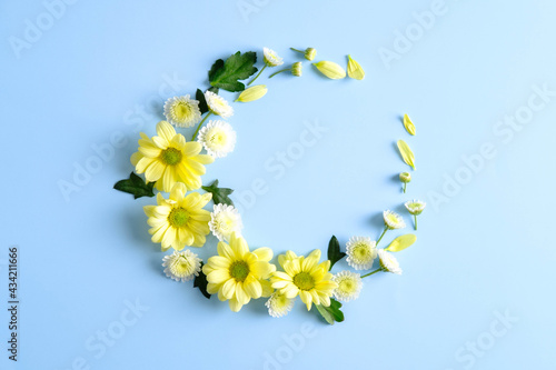 Round frame wreath with yellow flower buds and leaves on blue background. Flat lay, top view.