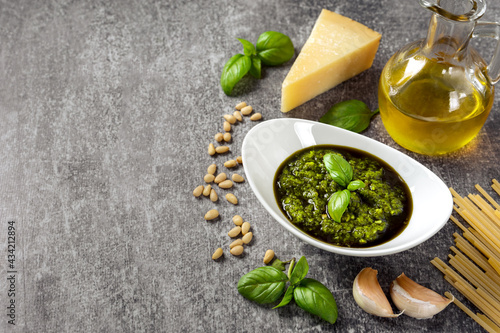 Homemade pesto sauсe with ingredients. Sauсe pesto in white bowl with basil, olive oil, pine nuts and parmesan cheese on gray concrete background with copy space for text.