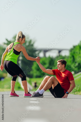 Attractive female helping her male running partner to get up from sitting on the running road track.