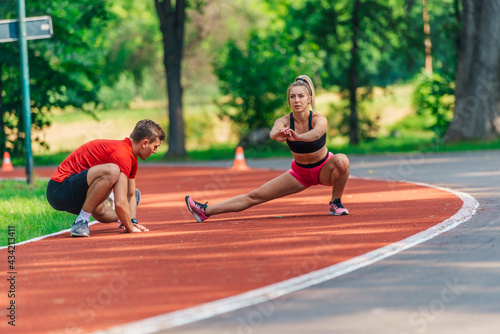 Attractive young couple stretching together on a race track after exercising outdoors