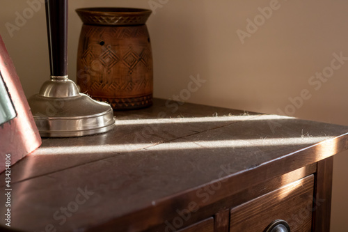 Layer of thick dust on top of a wooden side table and silver lamp.  photo