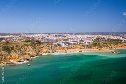 Fototapeta Naklejka Na Ścianę i Meble -  Dona Ana Beach in Lagos, Algarve - Portugal. Portuguese southern golden coast cliffs. Aerial view with city in the background.