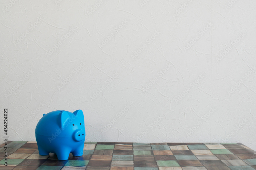 Fototapeta premium Blue Piggy Bank on Wooden Table with White Wall Background