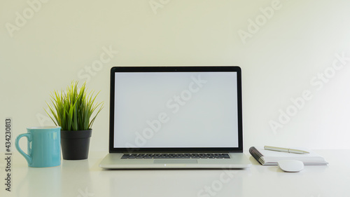 A laptop and a grass coffee mug with a notebook on the desk
