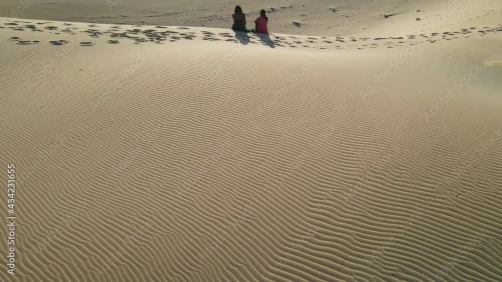 Drone flying over sand dunes with two people sitting at the edge