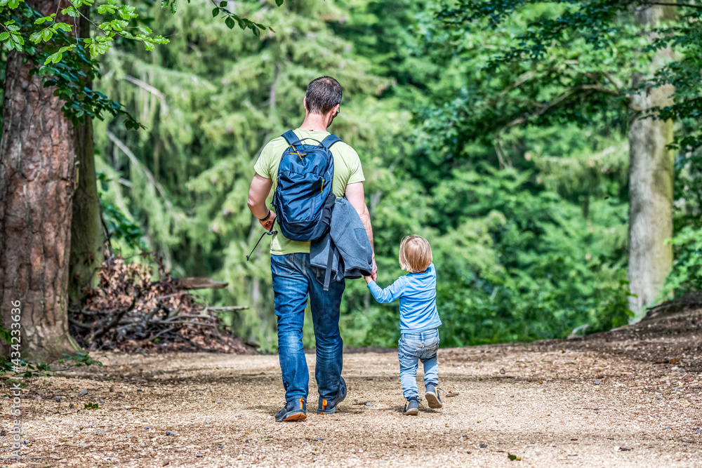 father holding hand of little son with backpack hiking in forest