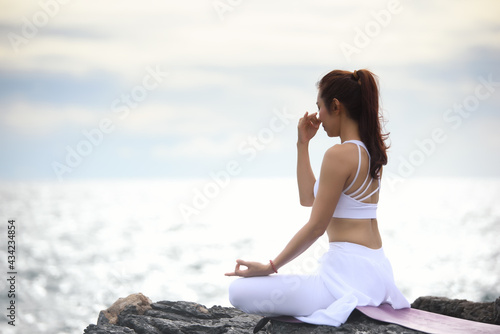 Asian young woman practicing yoga in sukhasana exercise while looking out to the sea. photo