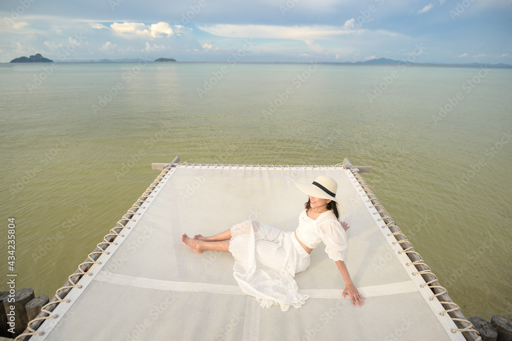 Obraz premium A happy beautiful woman in white dress enjoying and relaxing on terrace at the tropical island and turquoise clear ocean, Summer and holidays concept