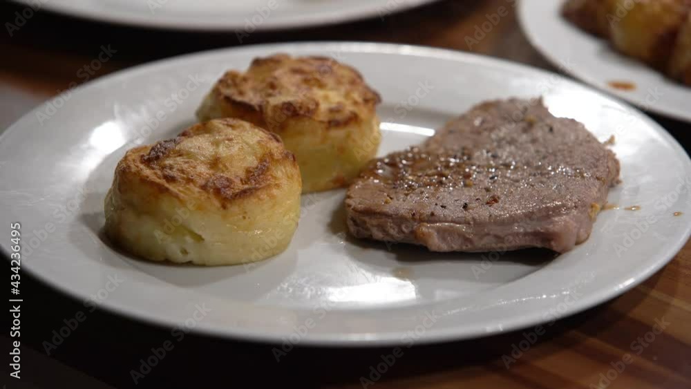 Grilled steak dish with potatoes cakes being added to the dish Grilled steak dish with potatoes cakes being added to the dish