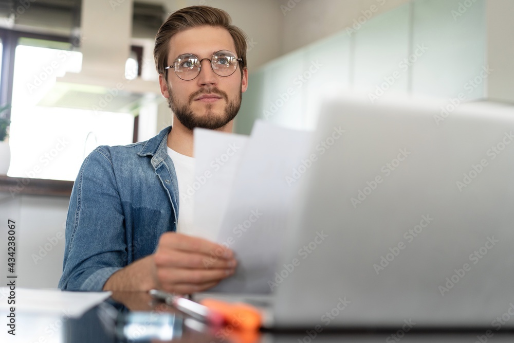 Young man working from home doing paperwork while using laptop. Young man working from home doing paperwork while using laptop.