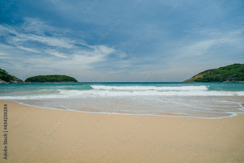 View of the beach with waves surrounded by green hills and white sand, turquoise water, bright sunny day