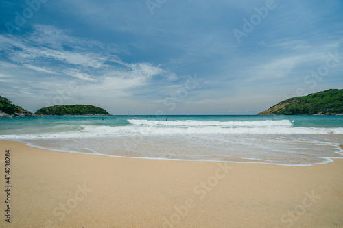 View of the beach with waves surrounded by green hills and white sand, turquoise water, bright sunny day