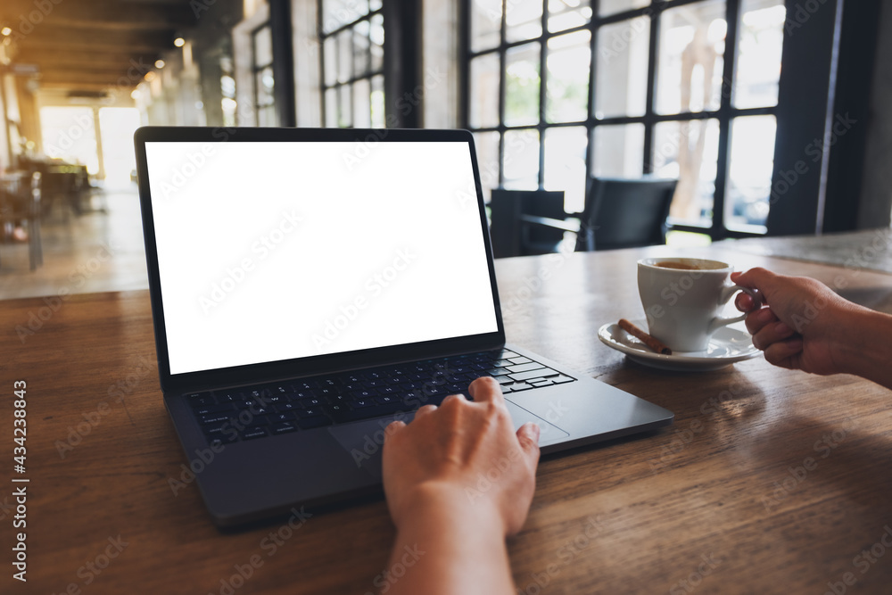 Fototapeta premium Mockup image of a woman using and touching on laptop touchpad with blank white desktop screen while drinking coffee