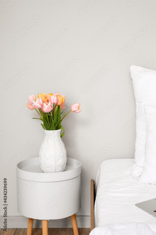 Tulip flowers on bedside table near white wall in room