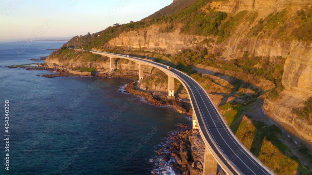 Sea Cliff Bridge During Golden Hour Of Sunrise With Mountain Cliffs In NSW, Australia. - aerial Sea Cliff Bridge During Golden Hour Of Sunrise With Mountain Cliffs In NSW, Australia. - aerial