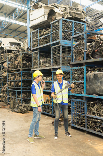 Men working together, One Asian engineer worker smile and show auto part to Colleague while he using walkie-talkie in factory-warehouse