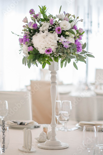 Centerpiece made of green leaves and fresh flowers stands on the dinner table. Wedding day. Fresh flowers decorations. © Mihai