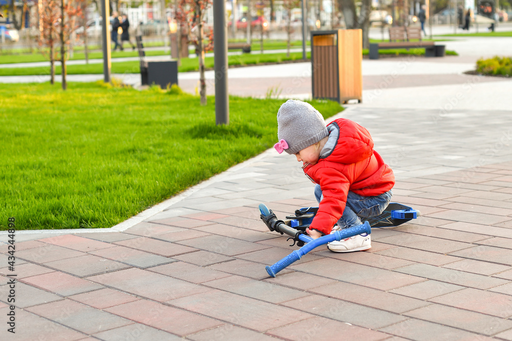 A small child fell from a scooter and is trying to climb, walking children in the park. A small child fell from a scooter and is trying to climb, walking children in the park.